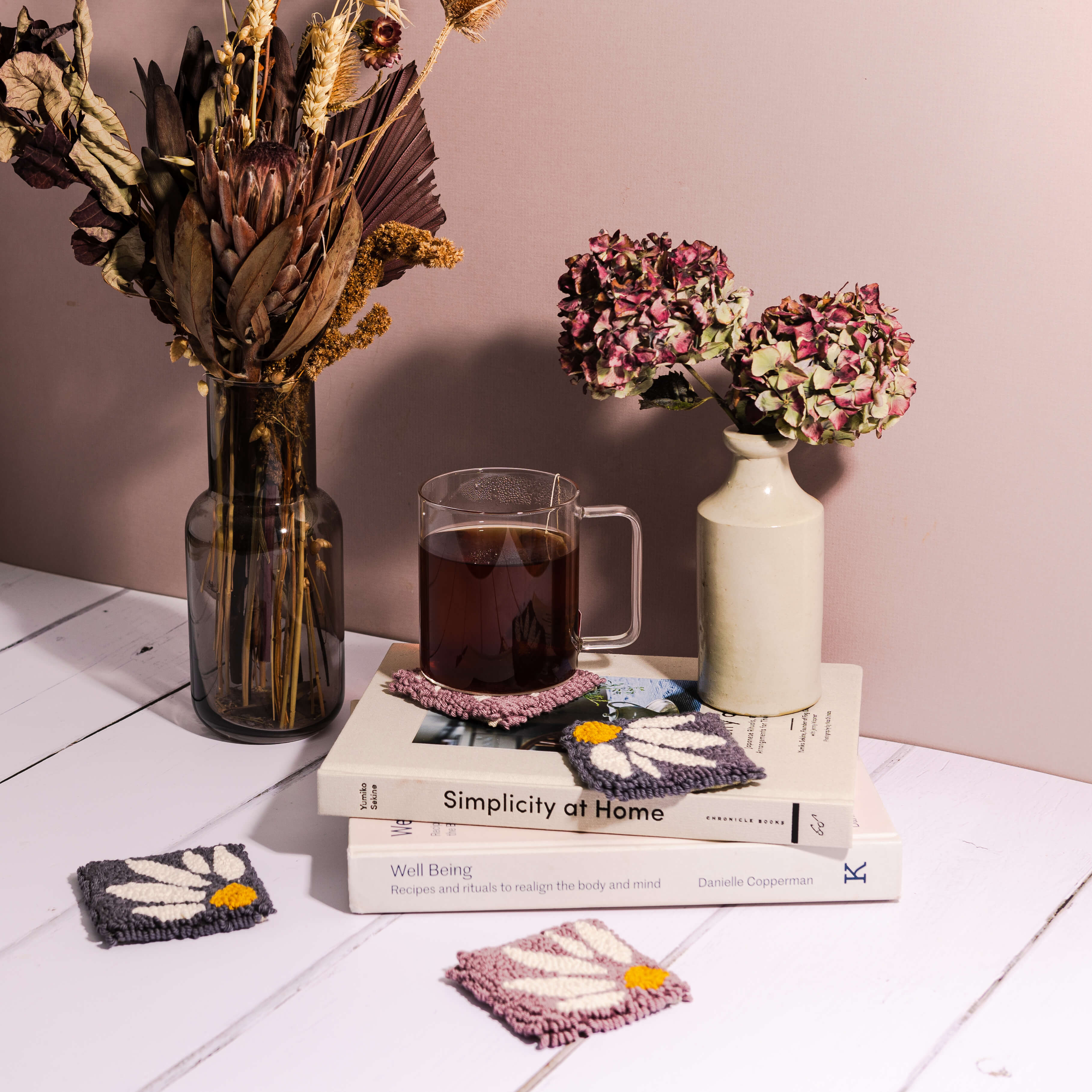 Lilac and dark grey floral punch needle coasters with books, vase and mug of tea propped on a coaster.